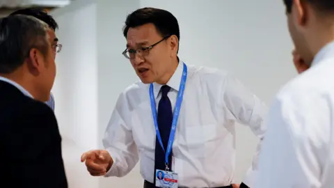 Reuters China's Vice Minister of Ecology and Environment Zhao Yingmin, in a white shirt, black tie and conference lanyard, points as he speaks with others at the COP29 United Nations Climate Change Conference, in Baku, Azerbaijan on 23 November