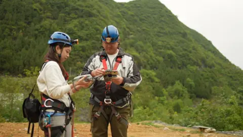 Xiqing Wang/BBC Rui and Michael in full gear, with blue helmets, prepare for their trek into the sinkhole  