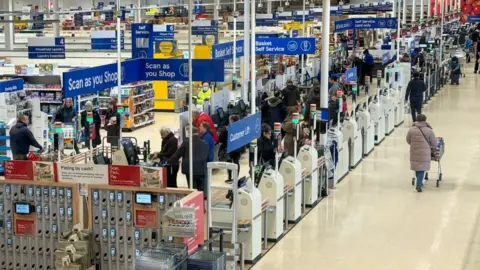 Getty Images People shop inside a large Tesco with Scan as you Shop signs and scanners and Self-service signs seen