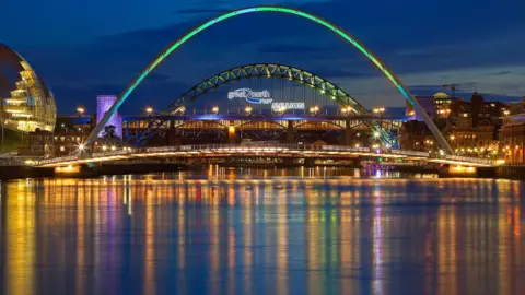 Getty Images The bright lights of Newcastle Upon Tyne at night - colourful lights are reflected in the still waters of the River Tyne. 