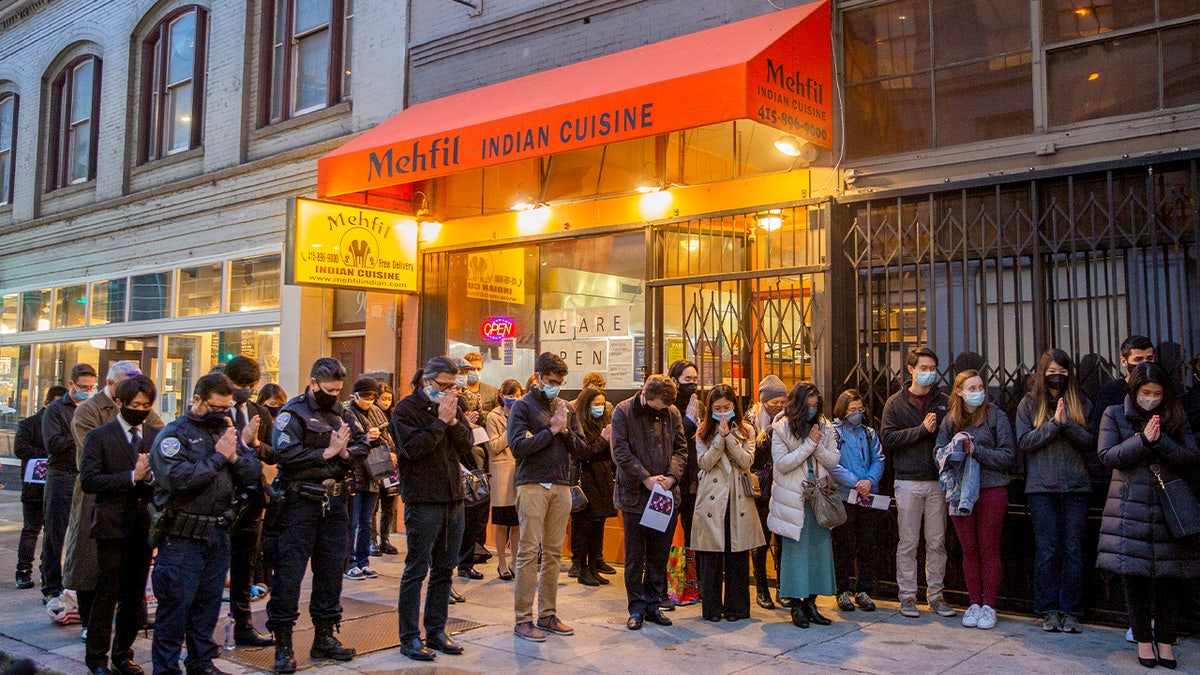 People gather for a memorial in front of a restaurant
