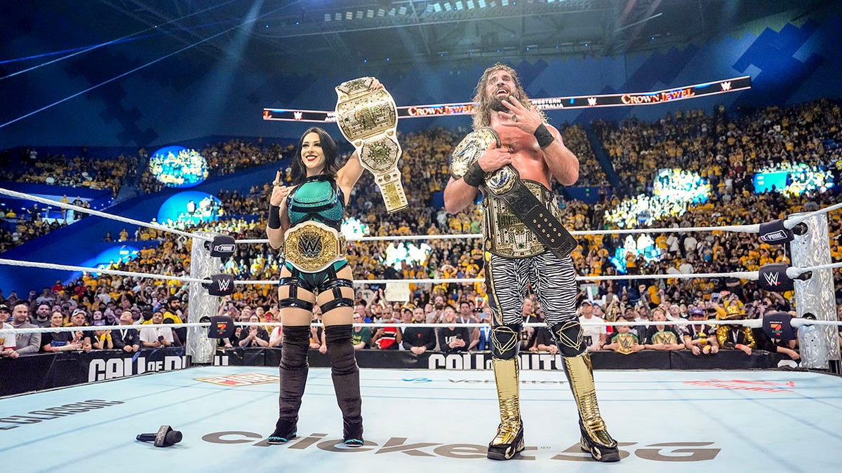 Stephanie Vaquer and Seth Rollins hold up their championships